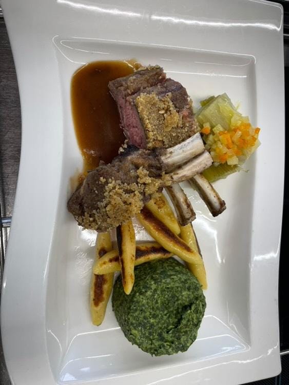 Lammkarree mit Kräuterkruste, Spinatpüree, Gnocchi und Gemüse auf weißem rechteckigem Teller.