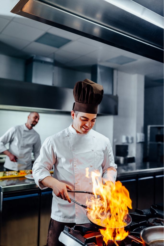 Der Koch flambiert das Gericht in einer Pfanne.